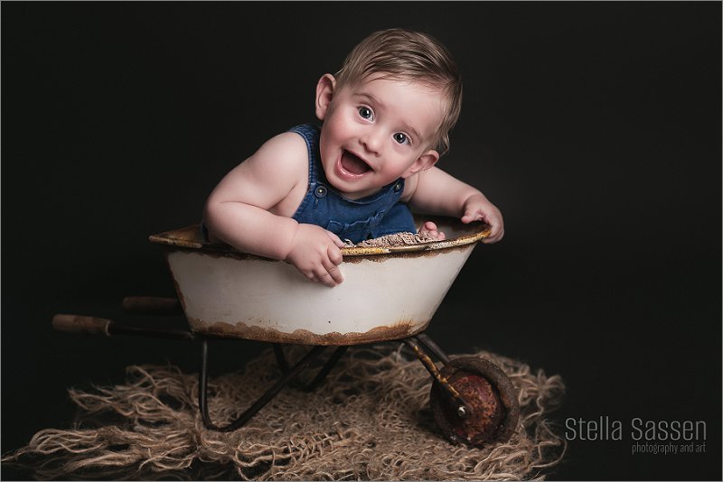 baby eight months old sitting and smiling in prop during photo shoot