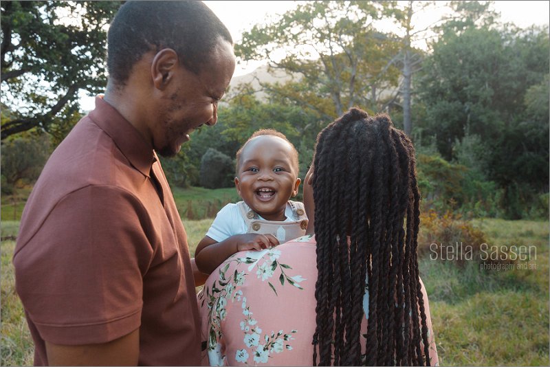 Joyful baby smiling as mom kisses him at photo session in forest