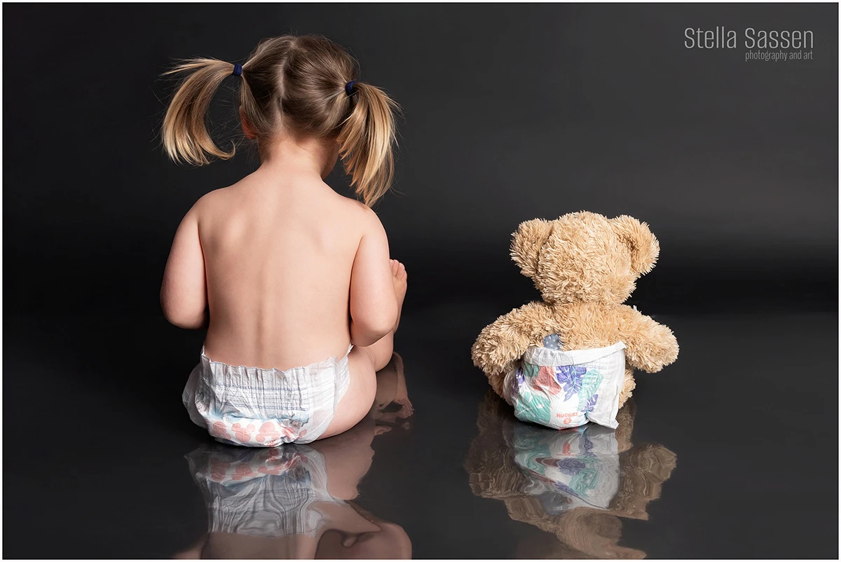 Toddler and teddy bear photographed from the back in photo studio