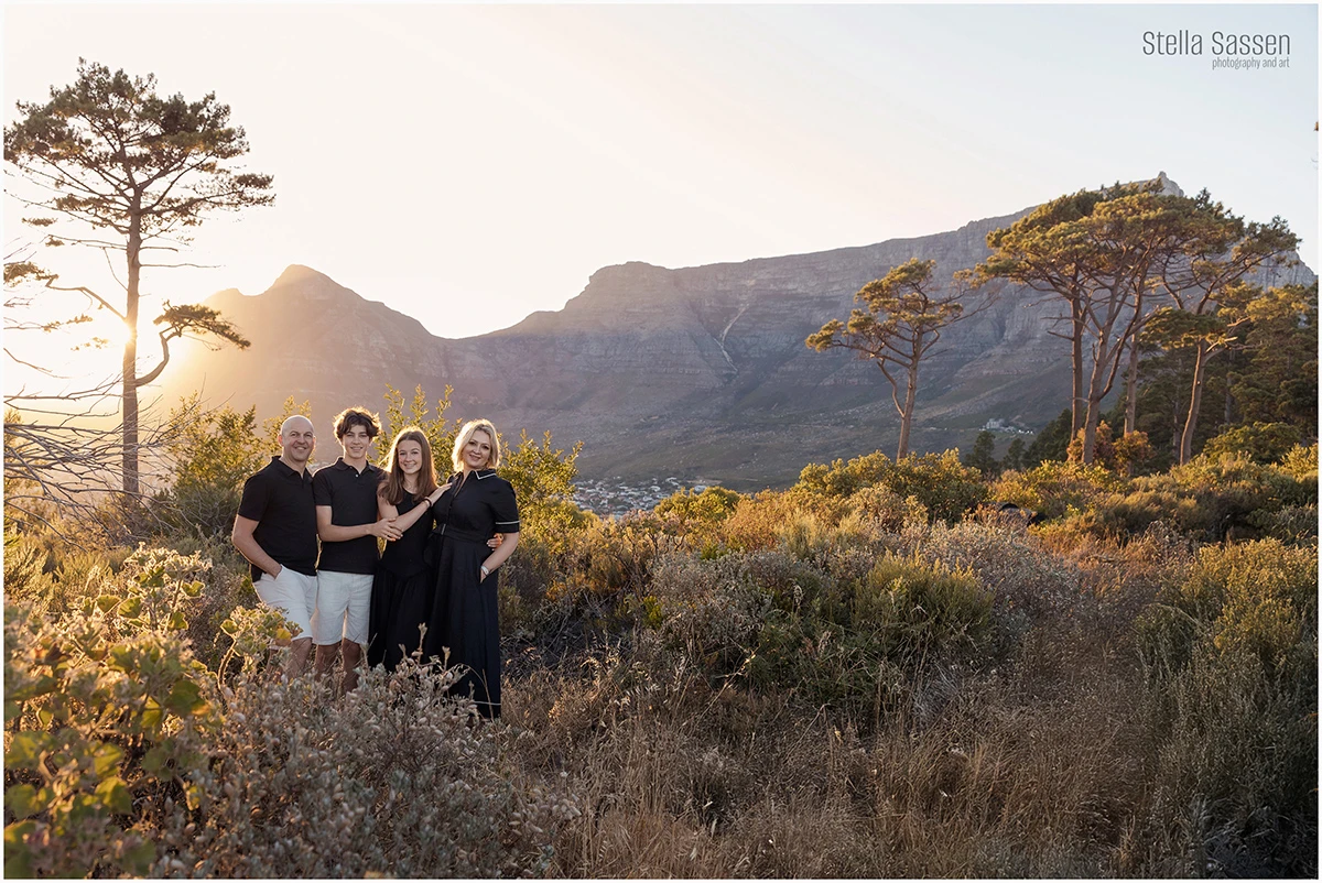 A family of four photographed at golden hour on Signal Hill, Cape Town, with Table Mountain and the city below visible in the background — all dressed in black against the warm sunset light.