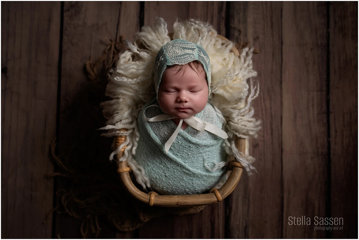 newborn baby in prop basket sleeping peacefully, wrapped in green with a green bonnet